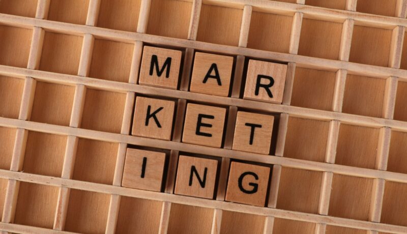 Wooden letter tiles spell out the word marketing on a grid background, showcasing creativity and business concept.