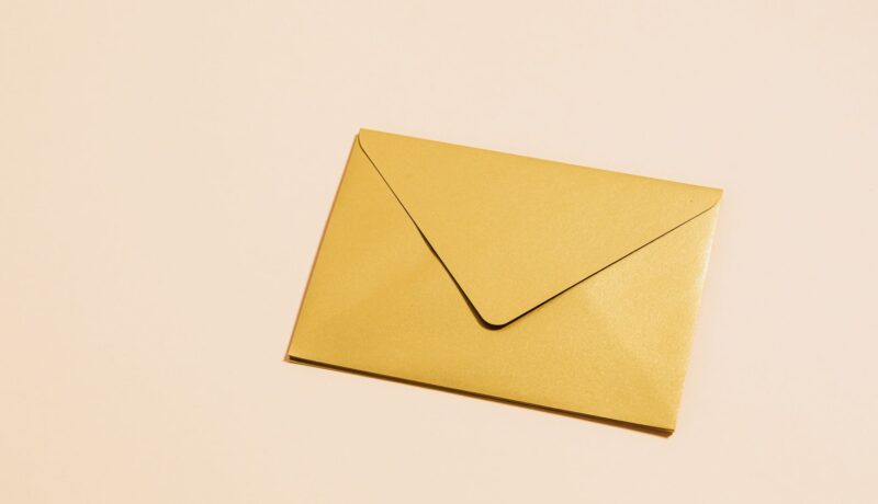 A sleek gold envelope placed on a vibrant yellow background, perfect for postal themes.