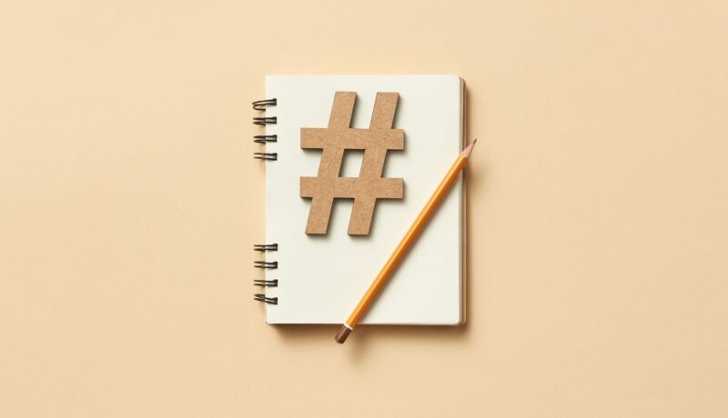 Minimalist flat lay featuring a notebook, hashtag symbol, and pencil on beige background.