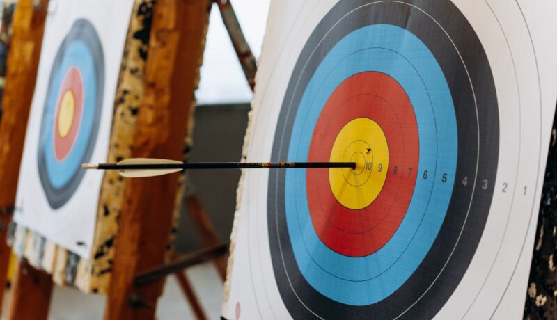 An arrow hits the bullseye on a colorful target in an indoor archery range.
