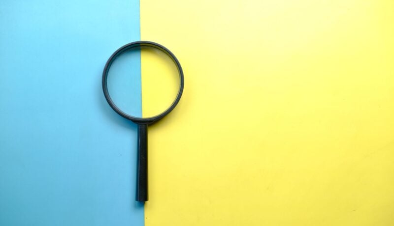 A magnifying glass lays on a split blue and yellow background in a flat lay style.