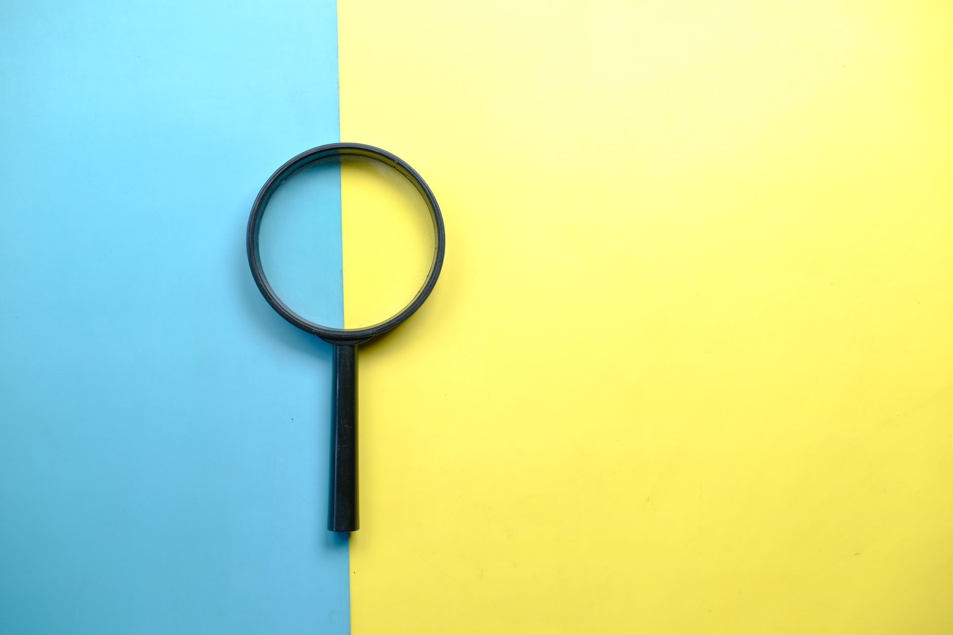 RevOps Attribution Models: Which One Fits Your Revenue Engine 1 A magnifying glass lays on a split blue and yellow background in a flat lay style.
