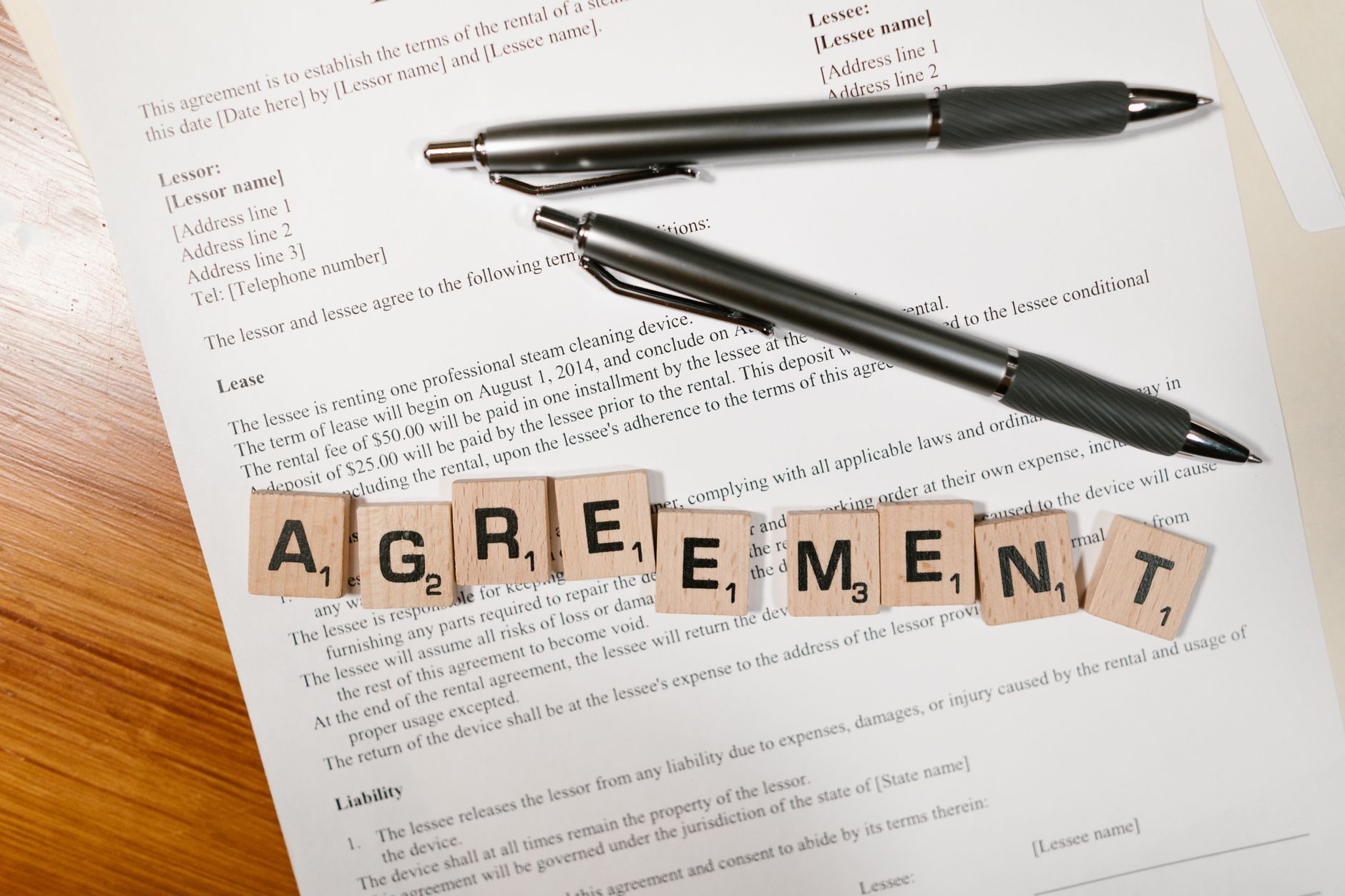 Sales and Marketing SLAs: Handoffs That Actually Convert Leads 1 A document with Scrabble tiles spelling 'AGREEMENT' and two pens, symbolizing contract signing.