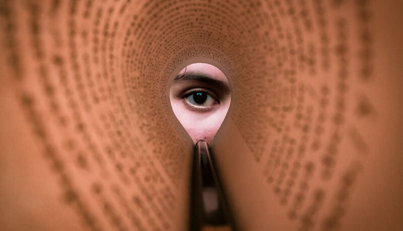 A person's eye looking through a rolled book page, creating a unique viewpoint.