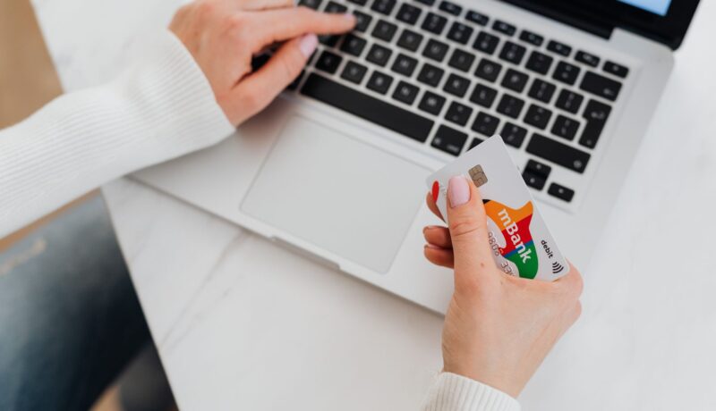 Close-up of a person using a laptop and holding a credit card for online shopping.