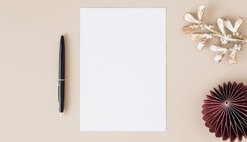 Elegant flatlay with blank paper, black pen, and decorative elements on beige.