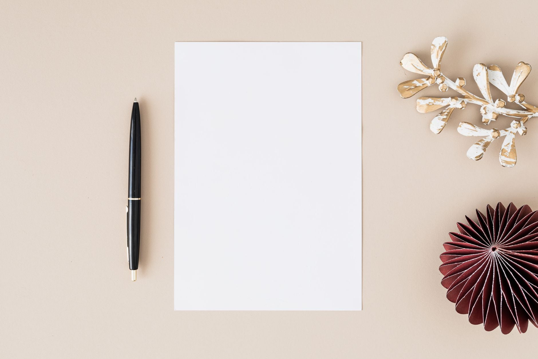 Elegant flatlay with blank paper, black pen, and decorative elements on beige.