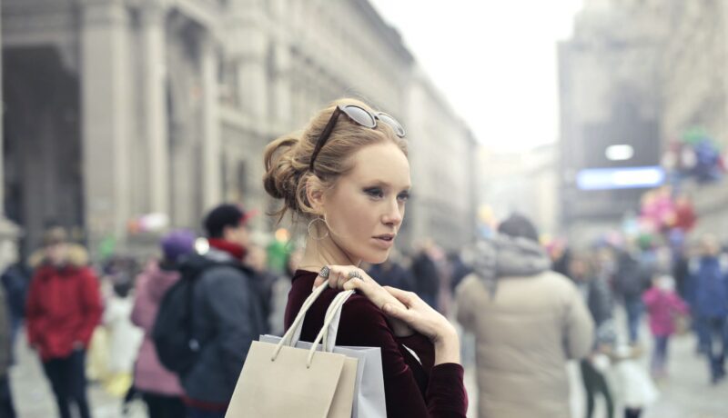 Stylish woman with shopping bags in bustling Milan street, embracing urban fashion vibes.
