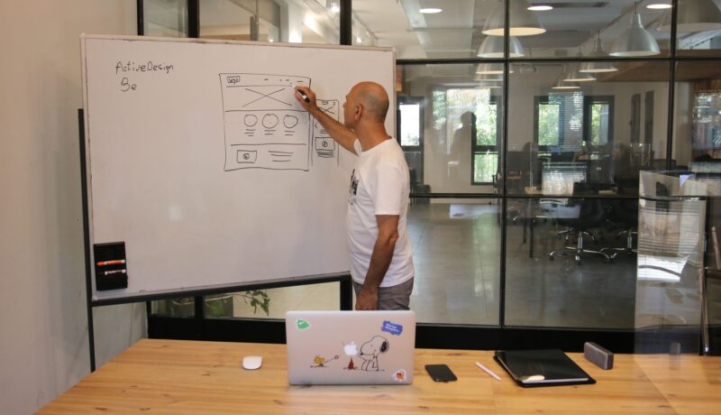 Side view of anonymous hairless male employee in white t shirt drawing draft on whiteboard while working on startup strategy in contemporary office